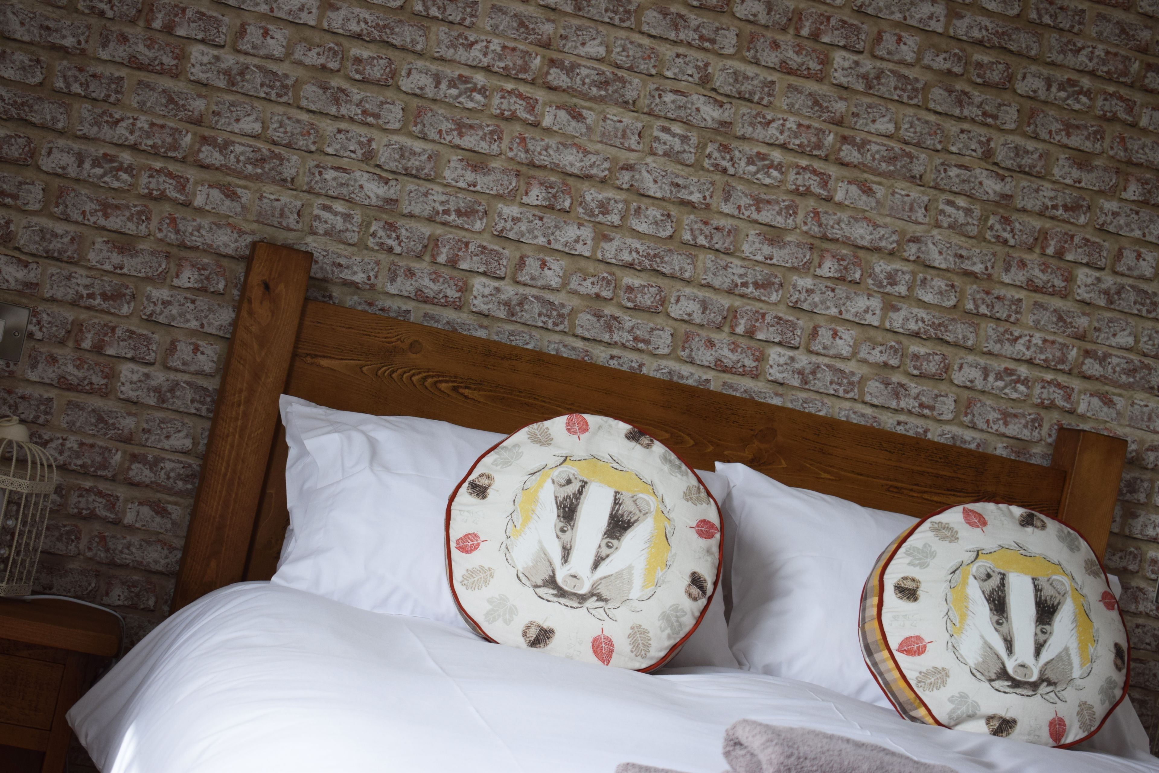 Una cama con ropa de cama blanca y dos almohadillas circulares con diseño de tejón.