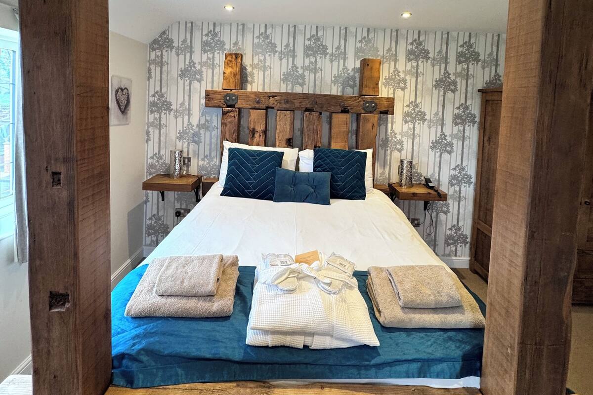 Uma cama com cabeceira de madeira, colcha azul e duas almofadas.