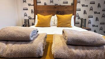 A bedroom with a wooden headboard, a bed with two pillows, and a patterned wallpaper.