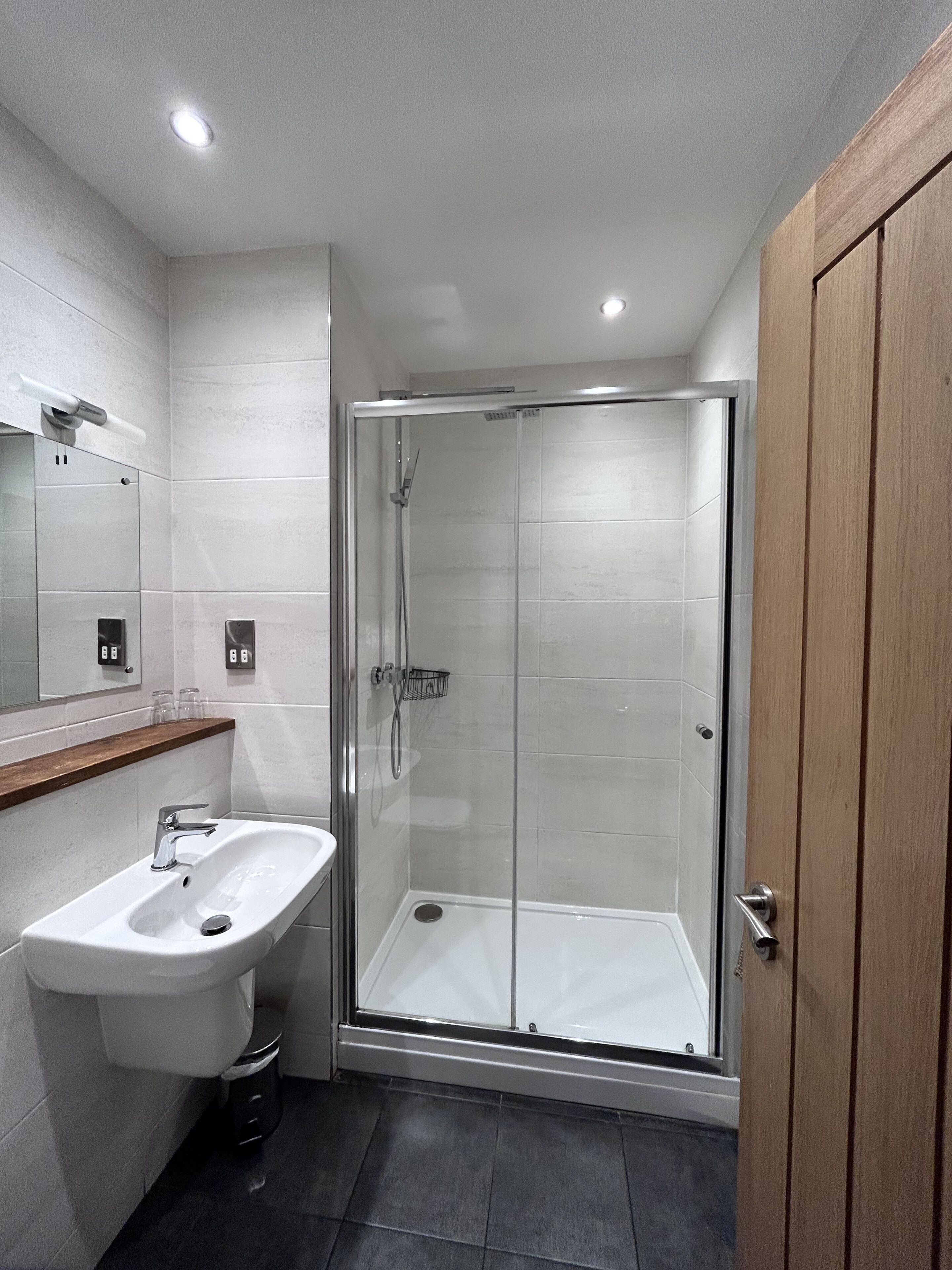 Un baño moderno con ducha envuelta en vidrio, un lavabo blanco y un mueble de tocador de madera.