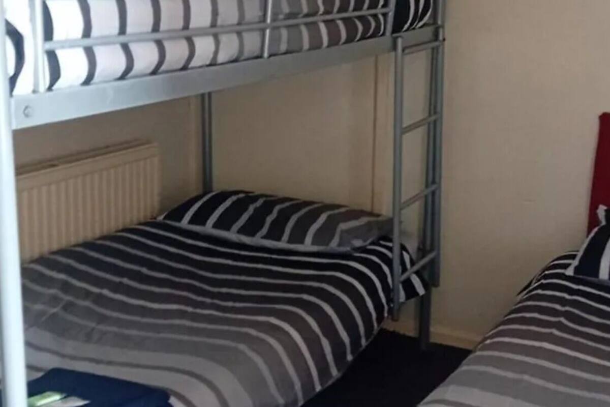 Habitación con literas, ropa de cama a rayas, cabecera roja y radiador.