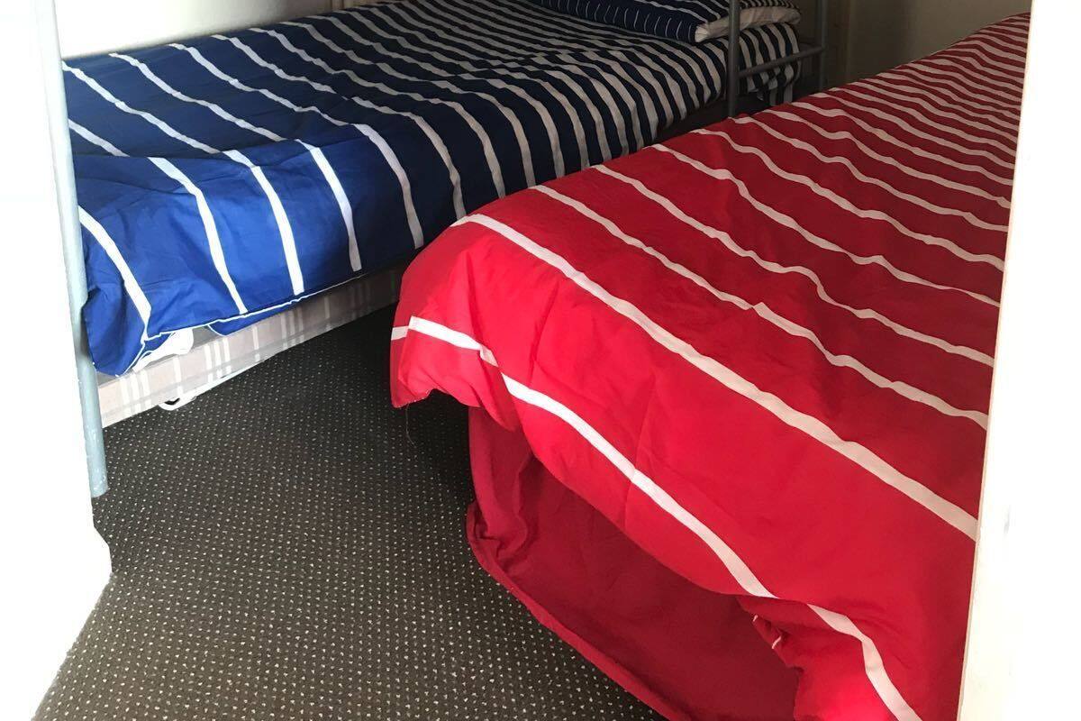 Una cama litera con ropa de cama azul y roja, un radiador y una puerta en una habitación.