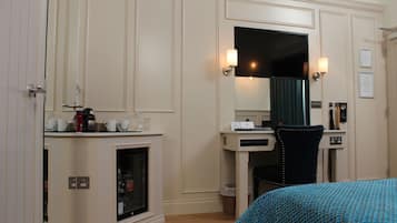 Habitación de hotel con cama, escritorio, silla, minibar y espejo.