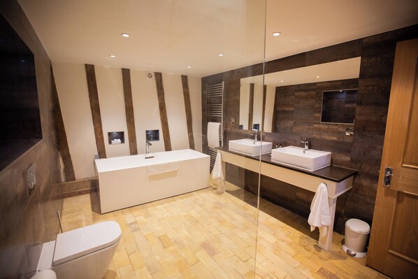 Un baño moderno con una bañera grande, dos lavamanos, un espejo y suelo de madera.