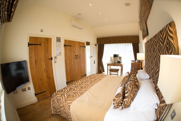 A hotel room with a large bed, a television, a desk with a lamp, and patterned curtains. - Channels Hotel (Chelmsford)