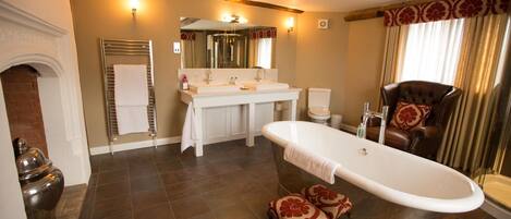A bathroom with a freestanding bathtub, a double sink vanity, and a leather armchair.
