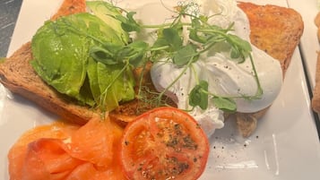 A plate with toast, avocado, smoked salmon, a tomato slice, and a dollop of cream cheese with greens.