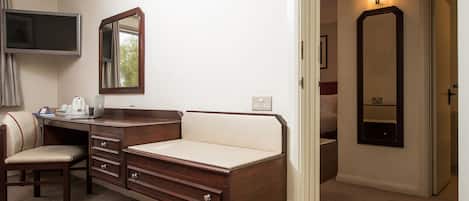 A hotel room with a desk, chair, and a bed. There is a television on the wall and a mirror above the bed.