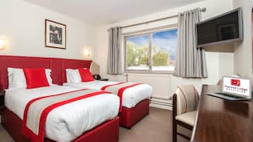 Ein Hotelzimmer mit zwei Betten, einem Schreibtisch, einem Fernseher und einem Fenster mit Vorhängen.
