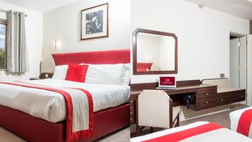 Habitación de hotel con una cama roja y blanca, un escritorio con una computadora portátil, un espejo y un cuadro en la pared.