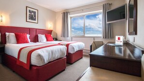 Habitación de hotel con dos camas, un escritorio, una silla, una ventana con vistas y un cartel con el nombre del hotel.