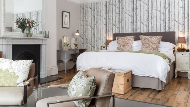 A bedroom with a large bed, a fireplace, a mirror, and a dresser. - Ravenhurst Bed and Breakfast (Cheltenham)