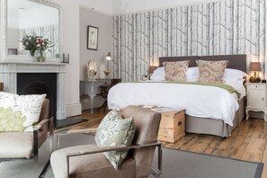 A bedroom with a large bed, a fireplace, a mirror, and a dresser.