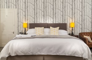 A neatly made bed with white bedding and two pillows, a brown headboard, and a wall with a tree pattern wallpaper. - Ravenhurst Bed and Breakfast (Cheltenham)