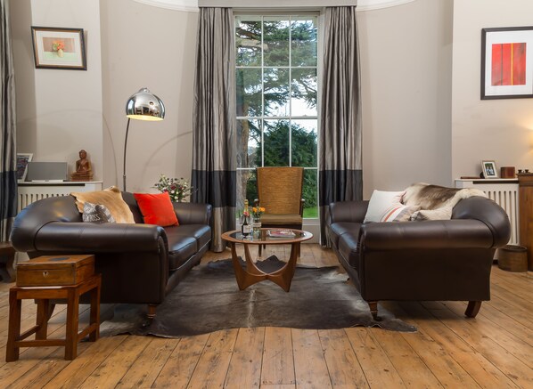 A living room with two leather sofas, a wooden coffee table, a floor lamp, and a view of greenery outside.