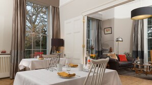 A dining area with white tables and chairs, a black sofa, and a wooden floor. - Ravenhurst Bed and Breakfast (Cheltenham)