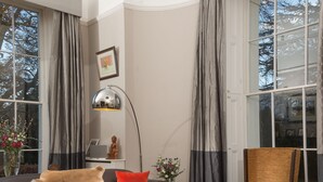 A modern living room with leather sofas, a round coffee table, and a large window with curtains. - Ravenhurst Bed and Breakfast (Cheltenham)