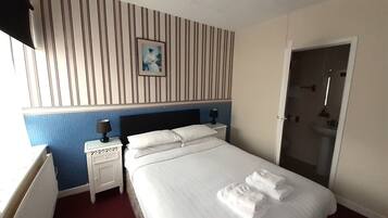 Habitación de hotel con cama, dos mesitas de noche, una mesita auxiliar, un cuadro enmarcado en la pared y un baño visible a través de una puerta abierta.