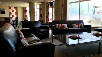 A modern living room with a black leather sofa, a glass coffee table, and black leather armchairs.