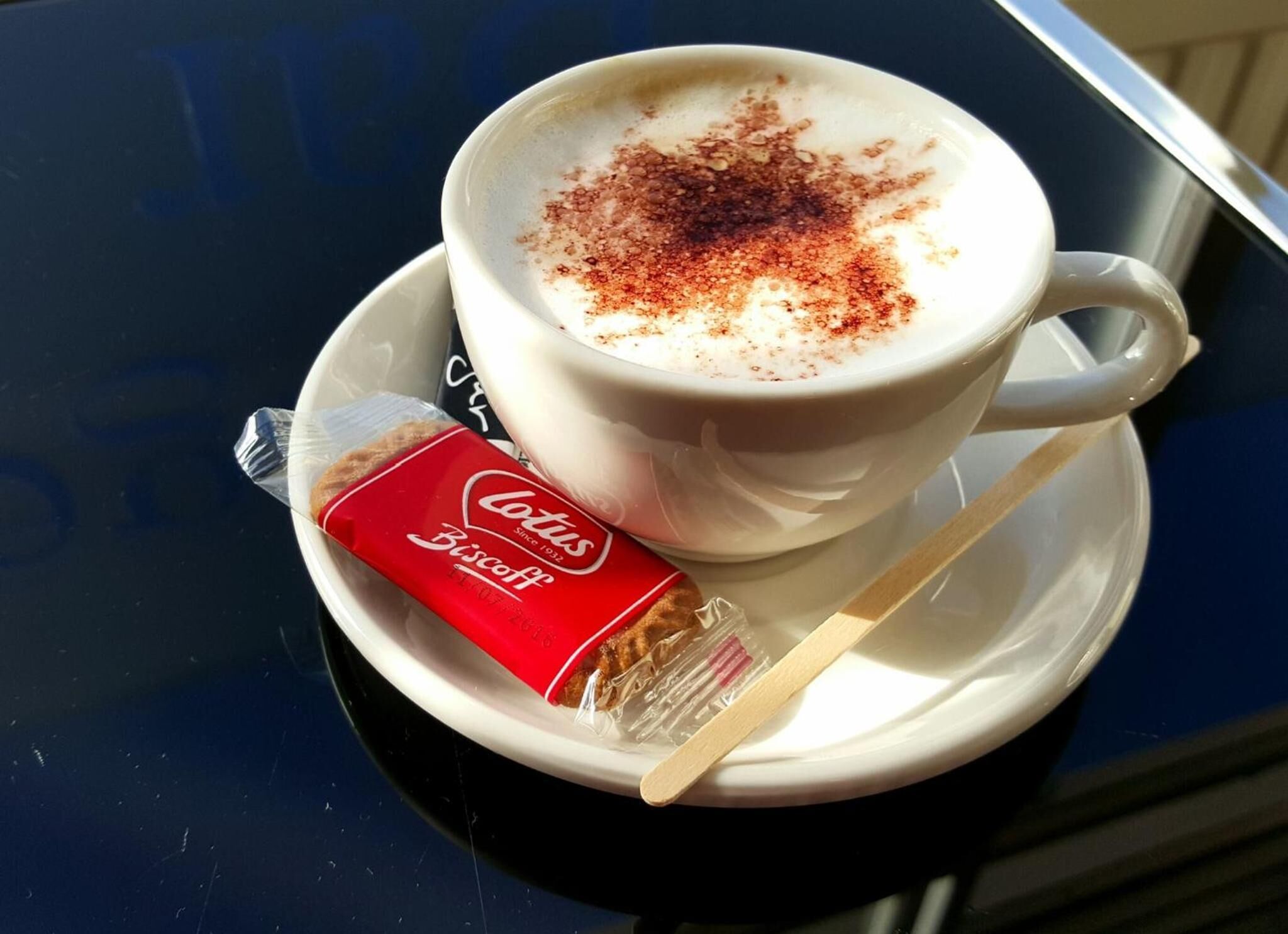 Een kop koffie met een beetje kaneel op een schotel, een pakje koekjes en een lepel.