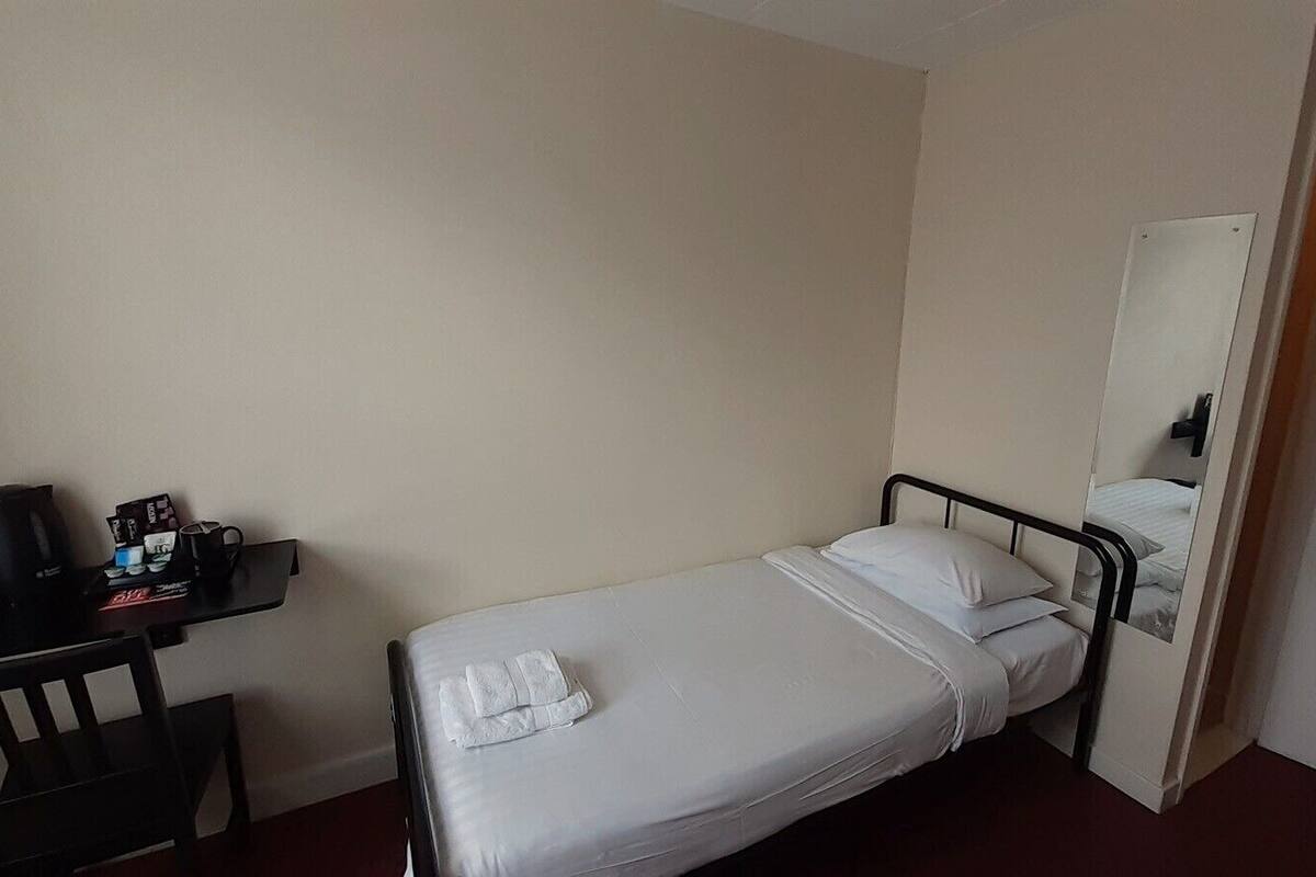 A small, single-bed room with a desk and chair, a coffee maker, and a mirror on the wall.