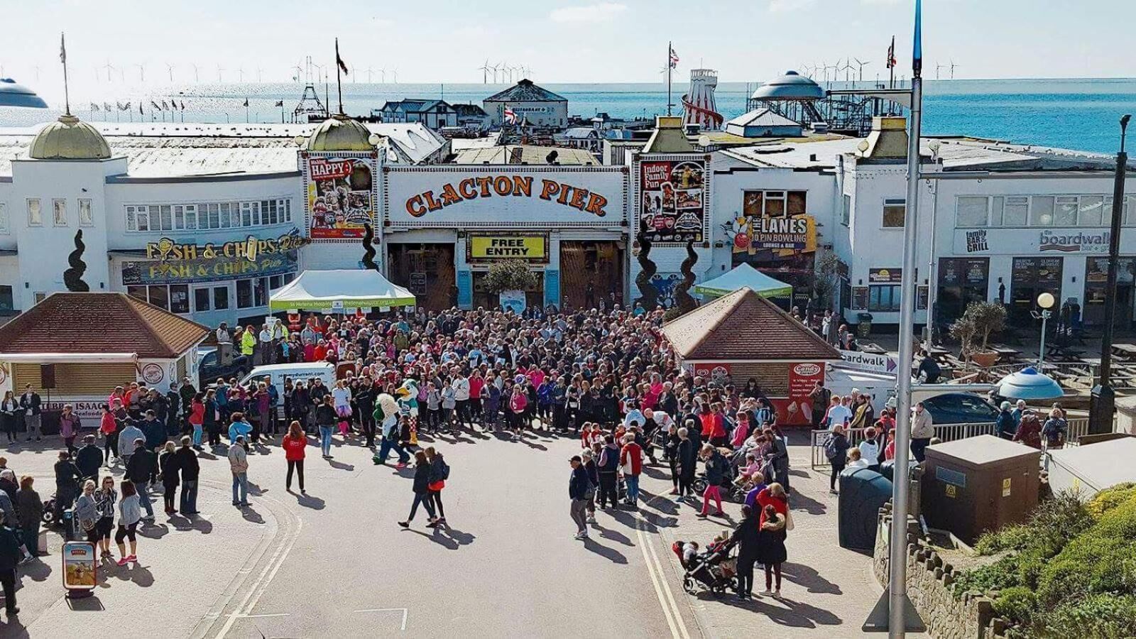Escena de calle concurrida con gente reunida frente a un edificio que dice 'CLACTON PIER'.