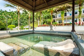A hot tub in a covered outdoor area with a pool, surrounded by palm trees and a building with balconies in the background. - Butchard Villas Sun Moon Lake (Yuchi)