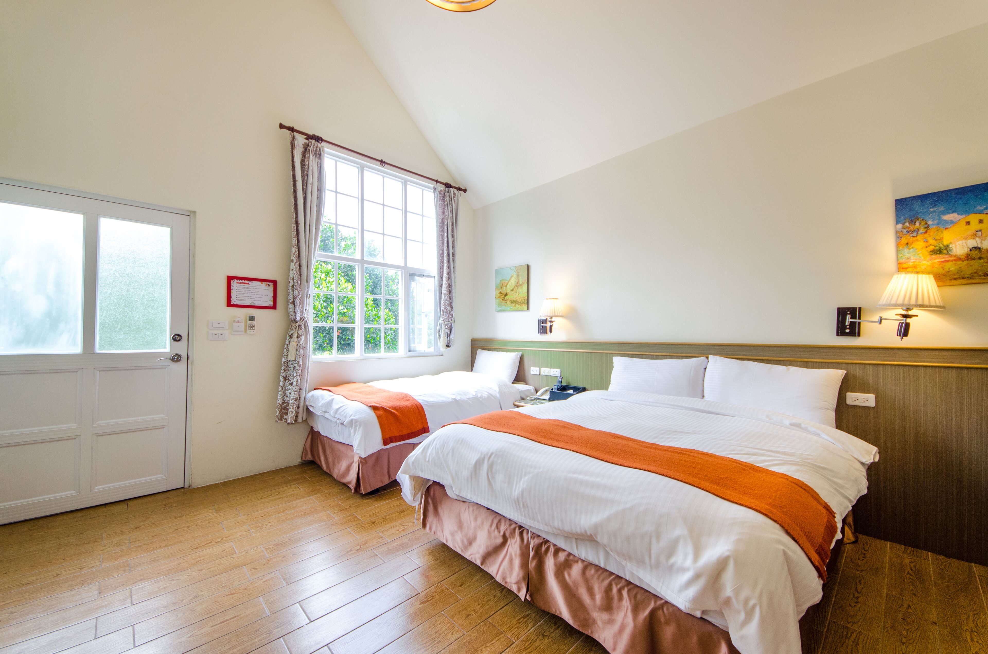 Een hotelkamer met twee bedden, een raam met gordijnen, een schilderij aan de muur en een lampje op het nachtkastje.