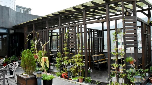 A covered outdoor seating area with wooden pergolas, potted plants, and outdoor furniture.