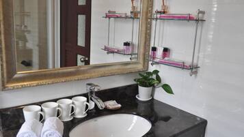 A bathroom with a large mirror, a white sink, and a marble countertop. There are towels and a potted plant on the counter.
