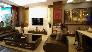 A modern living room with a flat-screen TV, leather sofas, a glass coffee table, and a dining area with chairs and a table.