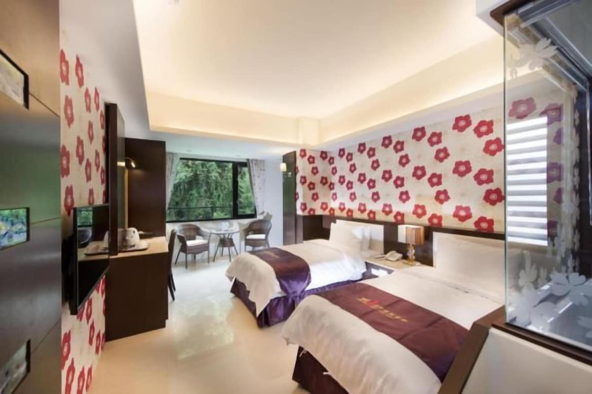 Quarto de hotel com uma cama grande, uma escrivaninha e uma cadeira. Há uma janela com vista para árvores.
