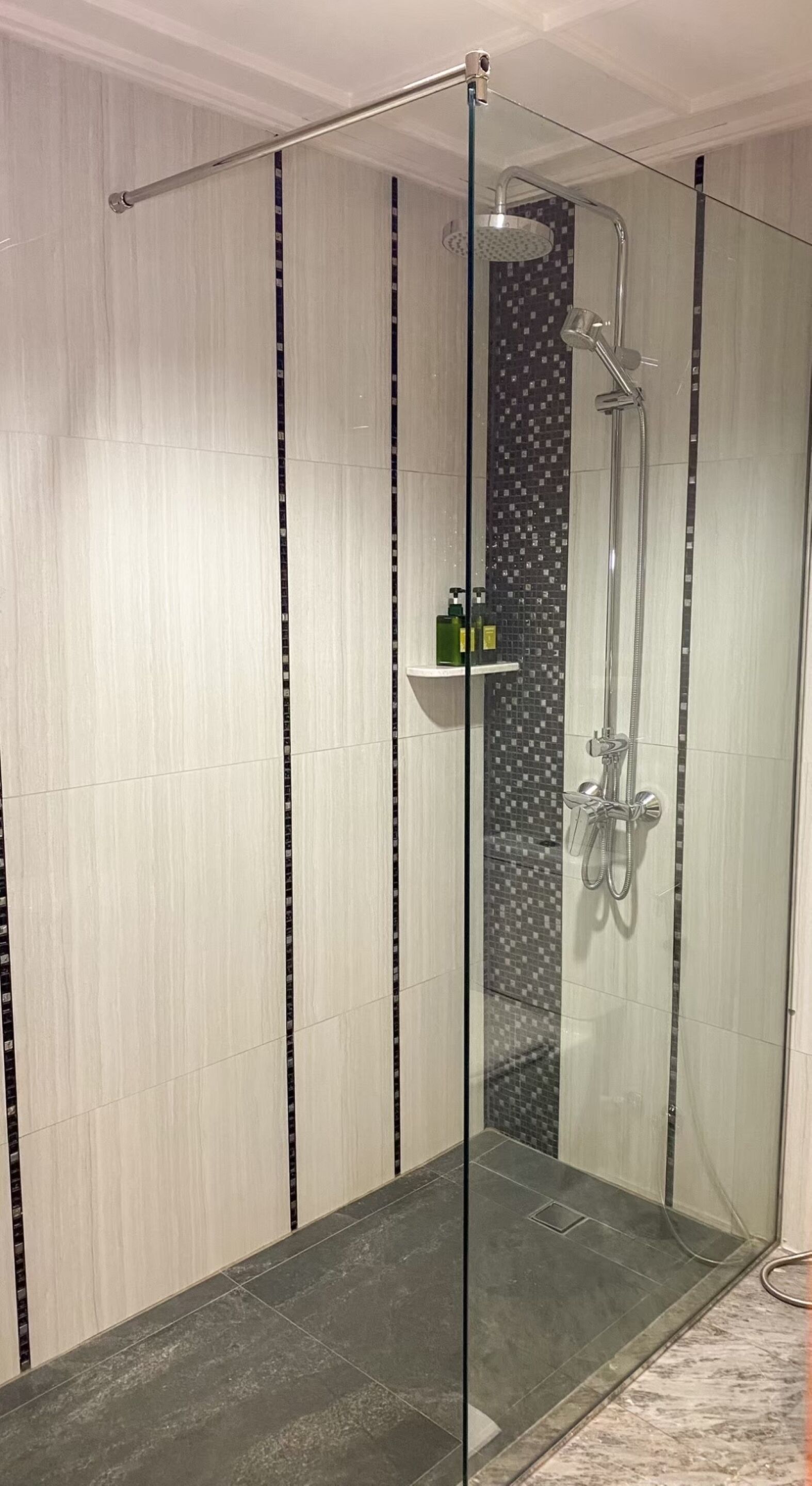 A glass-enclosed shower with a vertical black and white tile pattern on the wall.