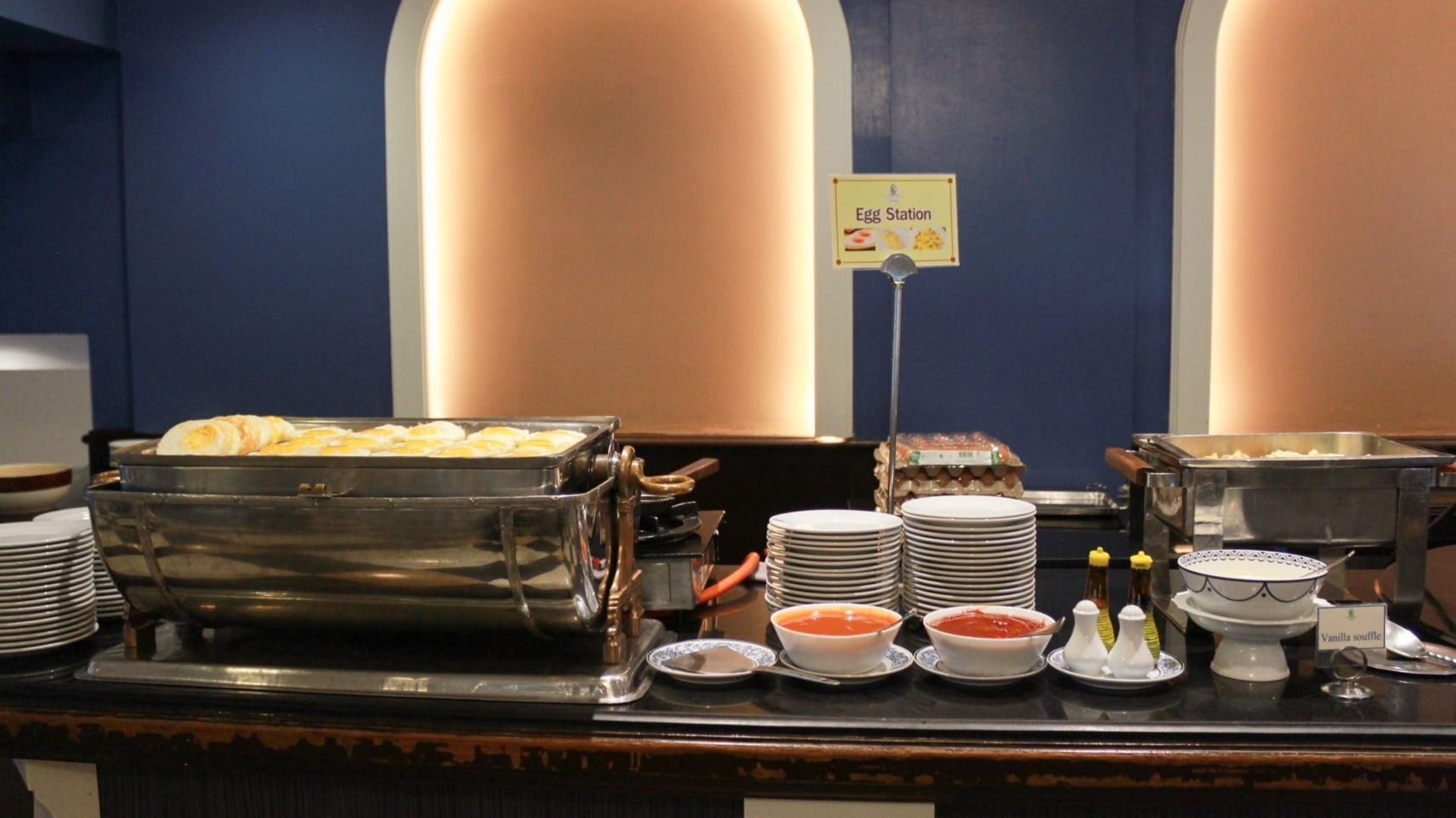 A buffet setup with various food items and condiments, including a sign for the egg station.