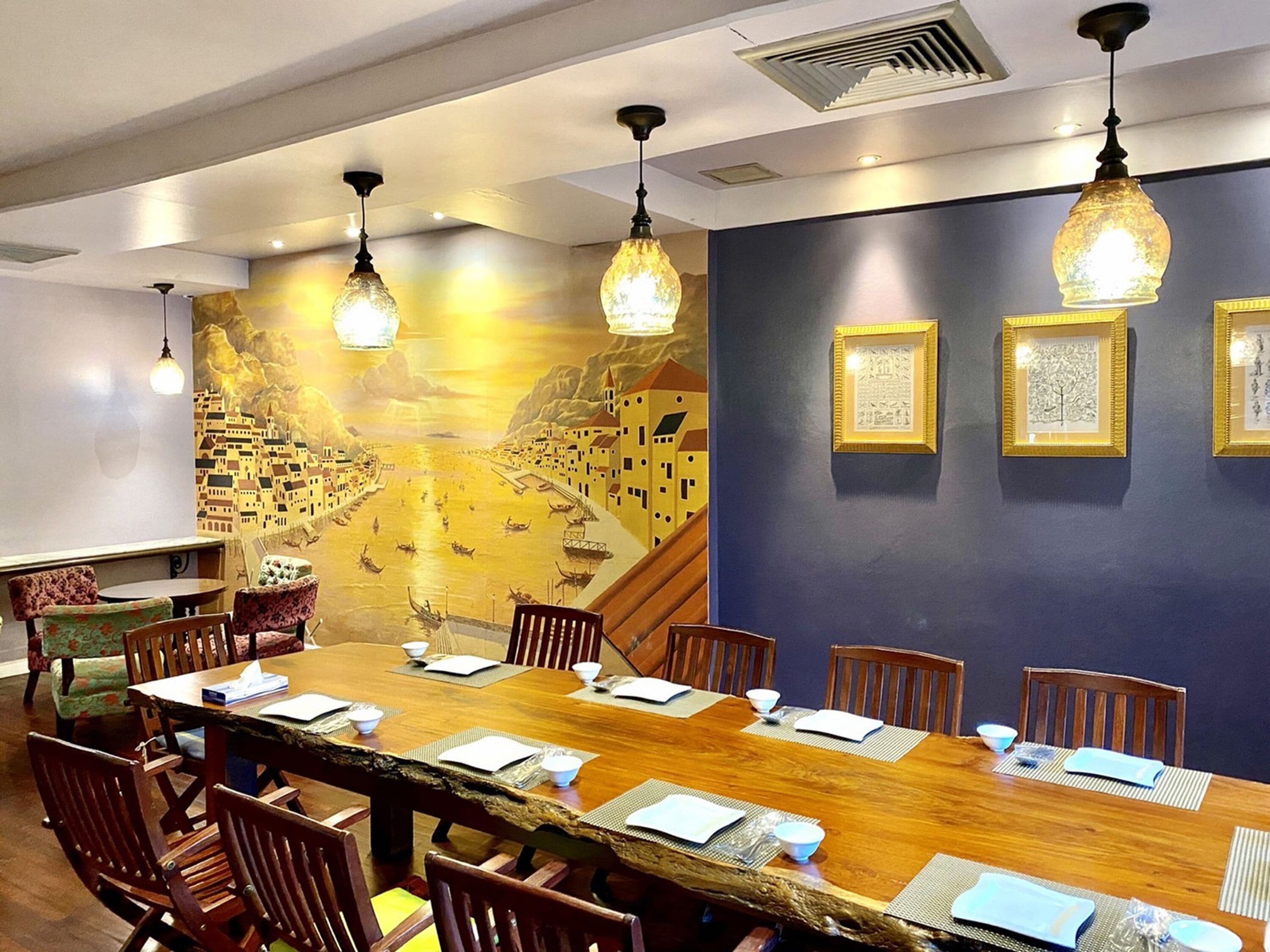 Un salón de conferencias con una larga mesa de madera, sillas y un mural de un pueblo costero.