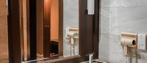 A modern bathroom with a granite countertop, a white sink, a large mirror, and a hairdryer mounted on the wall.