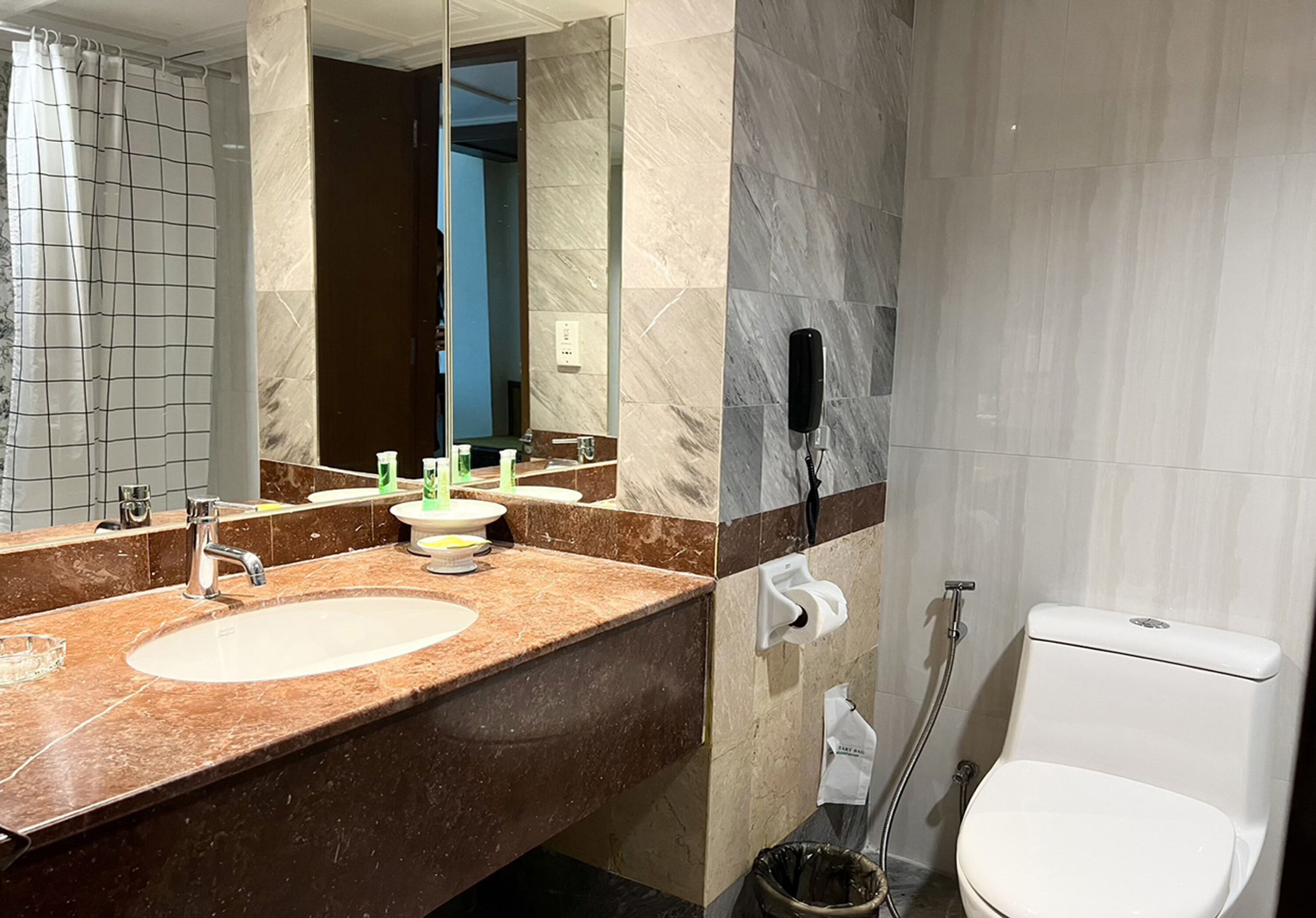 Un baño con lavamanos de mármol, dos espejos, un inodoro y zona de ducha.