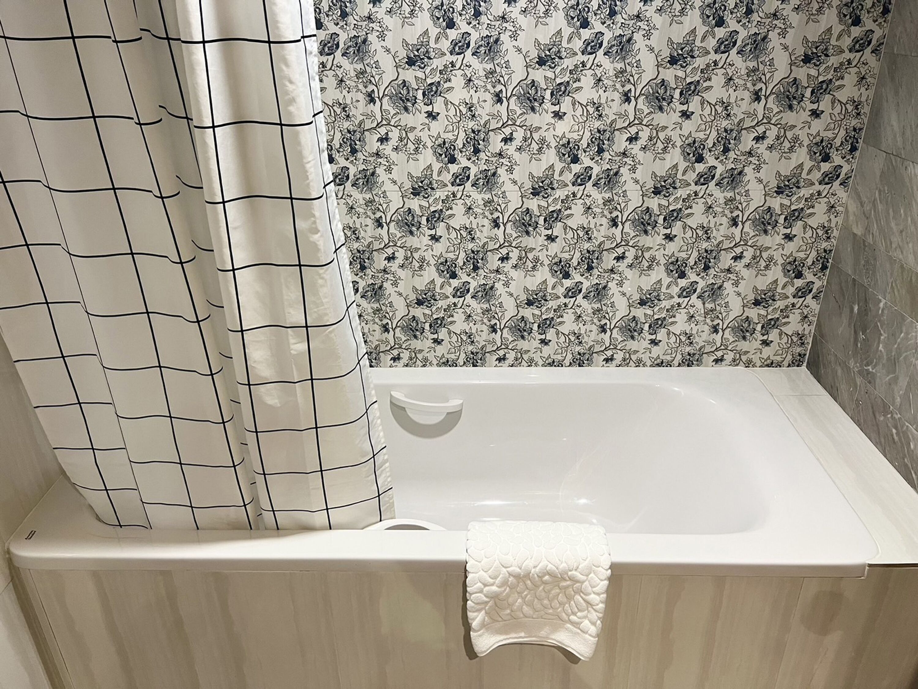 Et badeværelse med badekar, bruseforhæng og væg med blomstermønster.