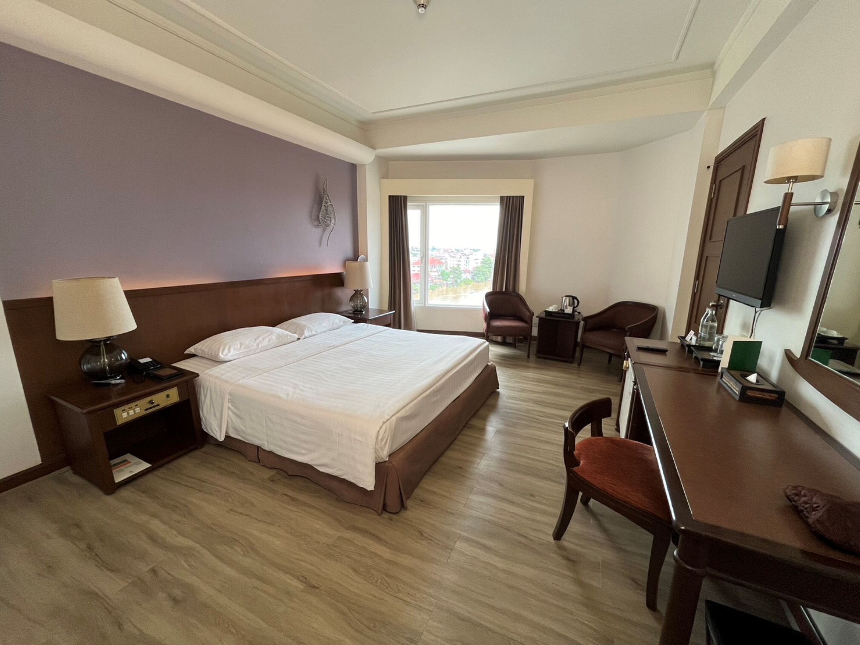 Habitación de hotel con una cama grande, un escritorio, una silla, un televisor y una ventana con cortinas.