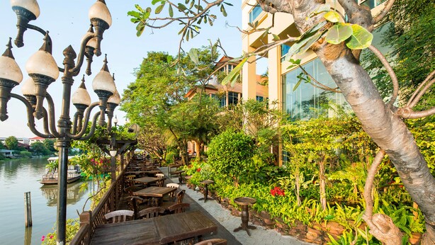 Un restaurante junto al río con terraza, mesas de madera y una fila de lámparas colgantes.