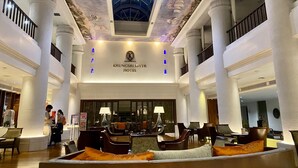 Un vestíbulo amplio con techos altos, grandes columnas y una zona de estar central con sofás y sillones.