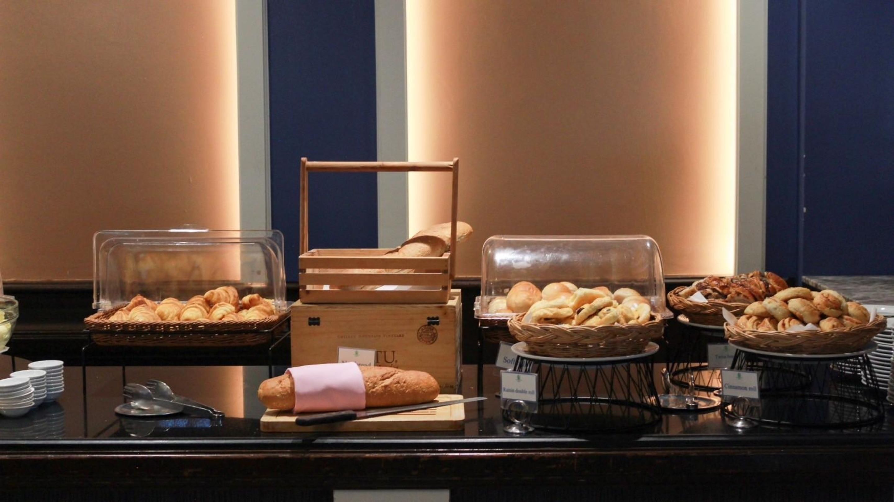 A buffet with various baked goods including bread, croissants, and pastries displayed in baskets and on a counter.