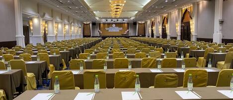A large conference room with rows of tables and chairs, equipped with water bottles and nameplates.