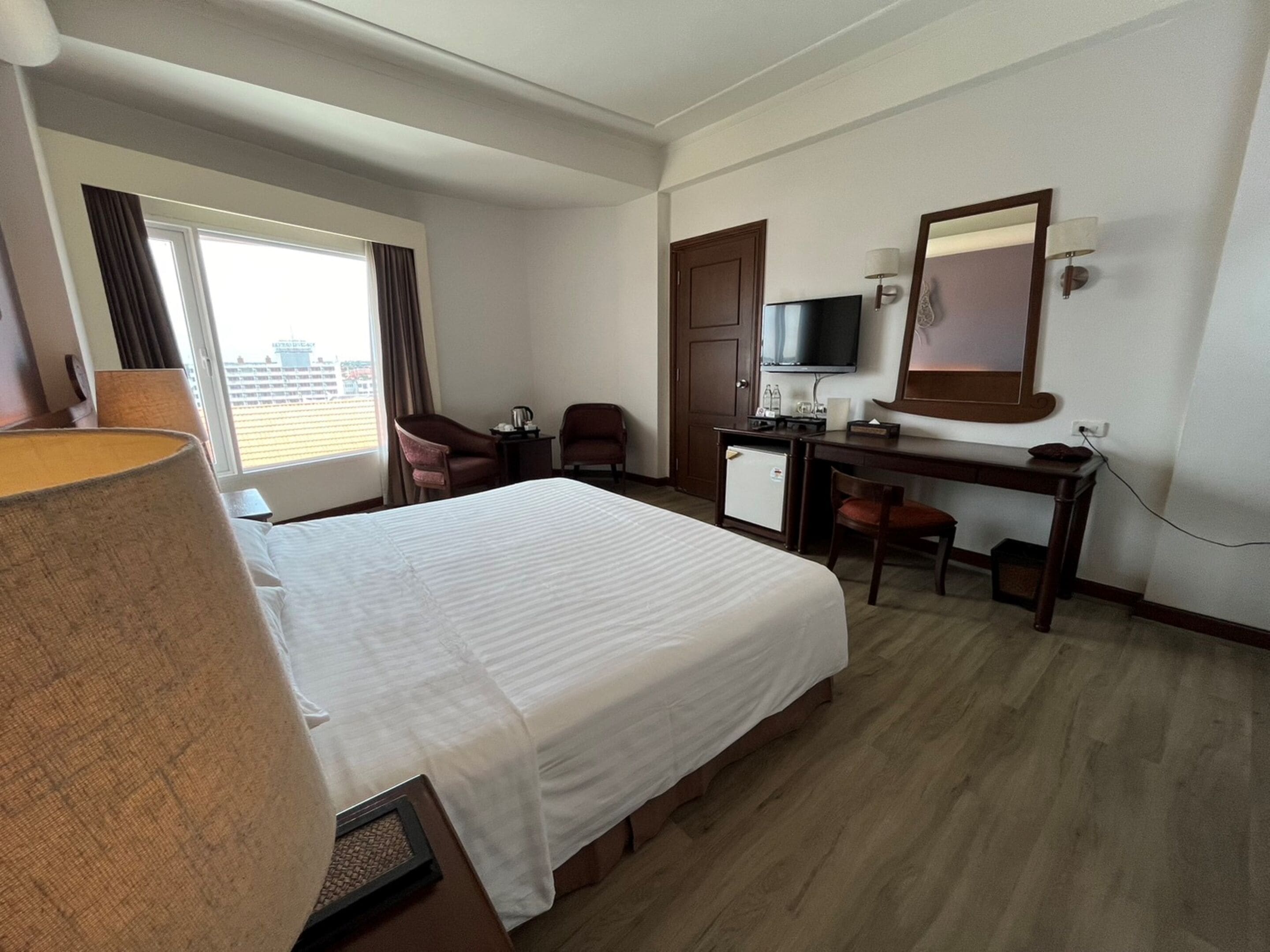 A hotel room with a large bed, a desk with a television, a chair, and a small refrigerator.