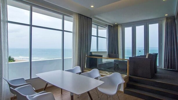 Een moderne hotelkamer met een groot balkon, een zithoek en een eethoek met uitzicht op de oceaan.