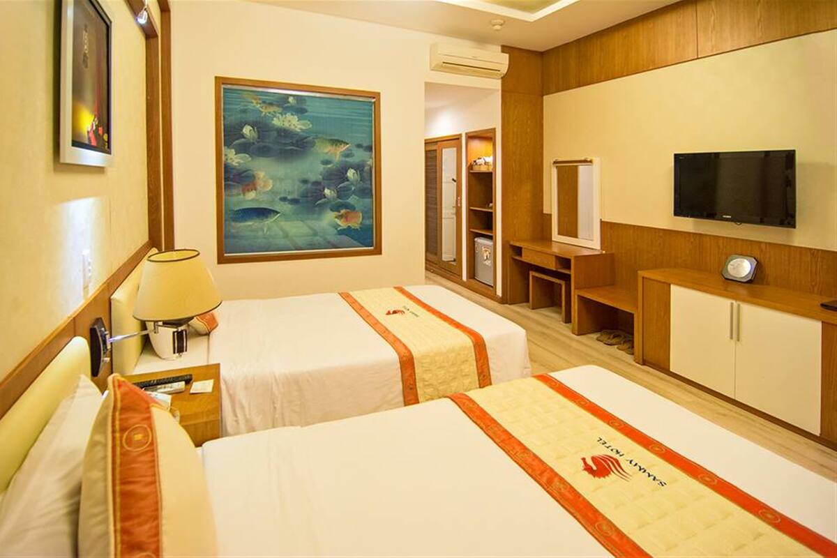 Ein Hotelzimmer mit zwei Betten, einem Gemälde, einem Fernseher und einer Minibar.