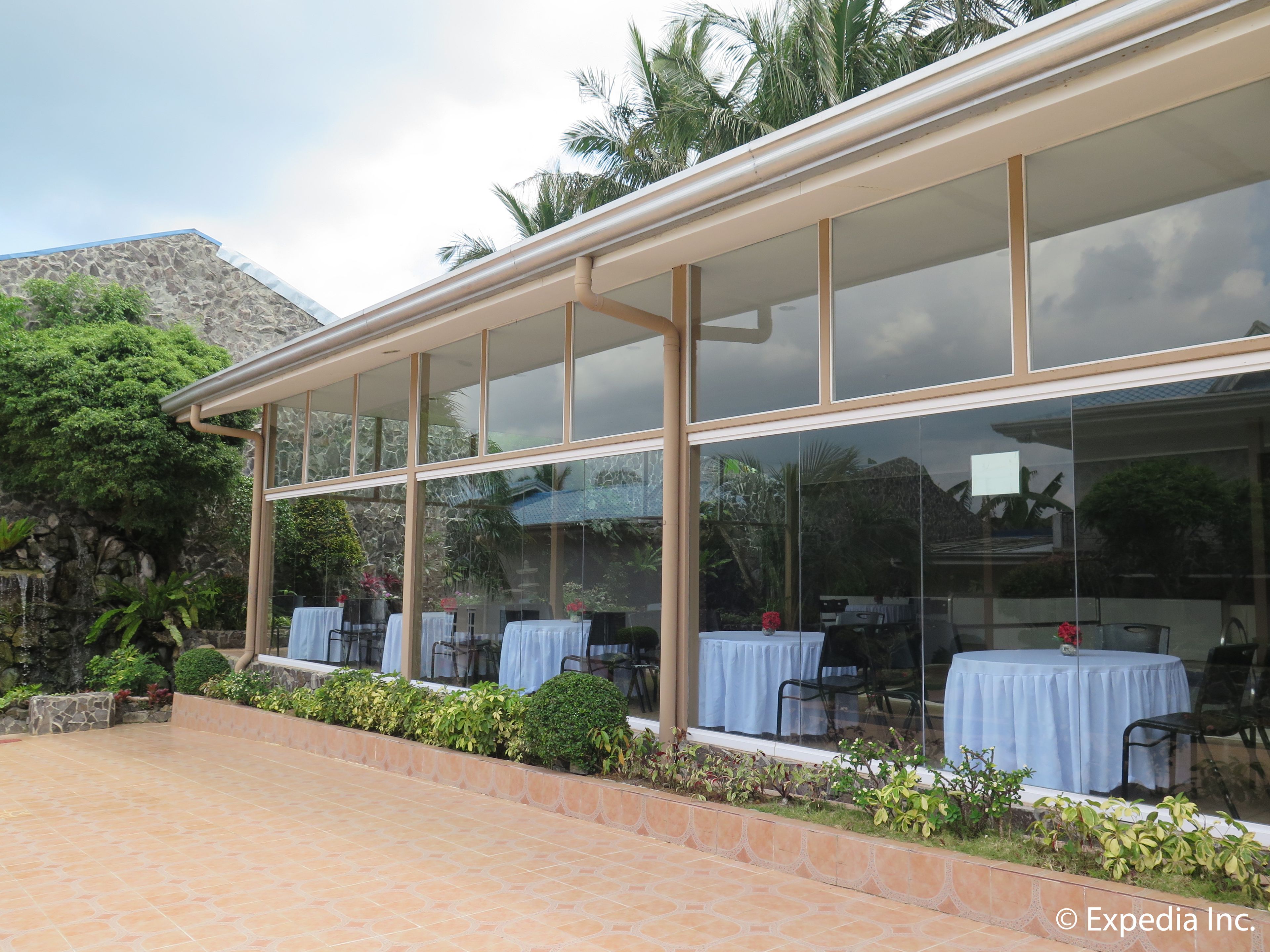 A restaurant with outdoor seating, large windows, and a stone wall backdrop.