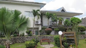 Un edificio residencial con un muro de piedra, una palmera, un banco de madera y un camino de piedra.