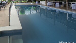 Una piscina interior con agua cristalina, rodeada de mesas y sillas, y un muro de piedra al fondo.