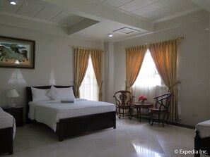 Une chambre d’hôtel avec un lit, une chaise, une petite table sur laquelle est posé un vase de fleurs, et un tableau accroché au mur.